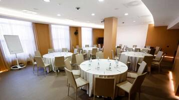 A conference room with multiple round tables, white chairs, and a whiteboard.