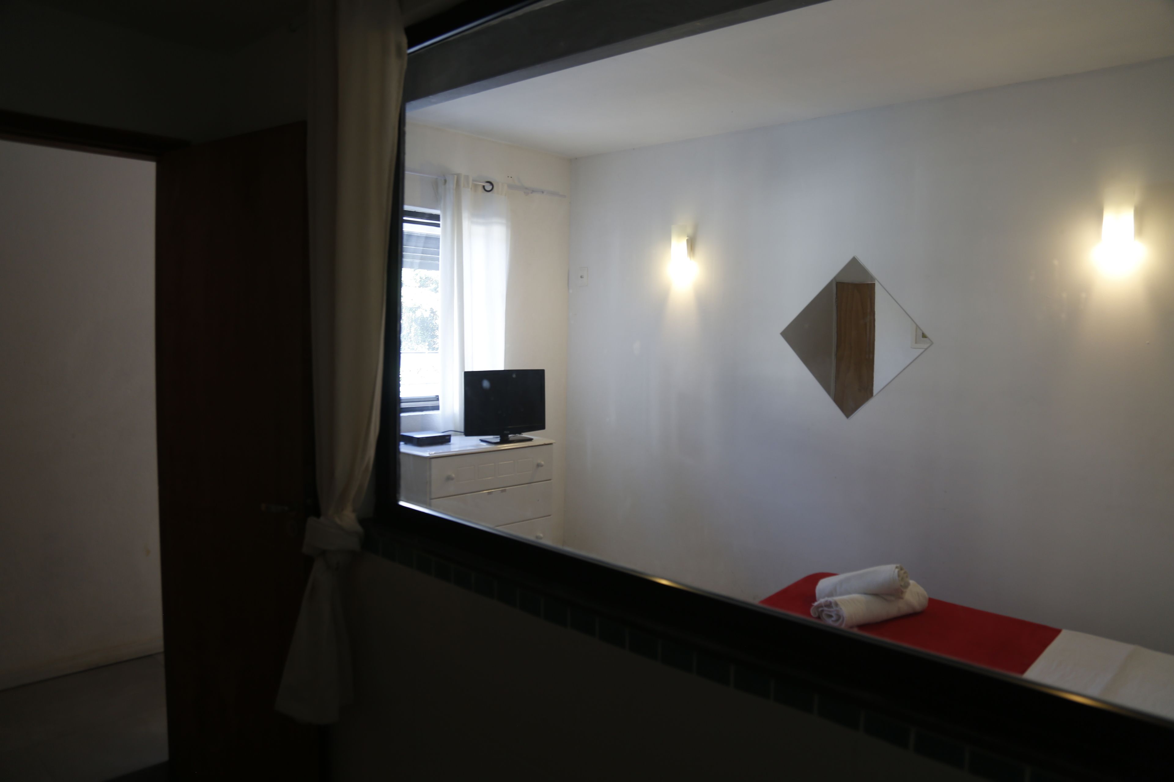 A hotel room with a bed, a TV on a dresser, a mirror on the wall, and a window with curtains.