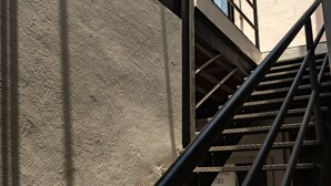 Una escalera con barandillas de metal y un muro de concreto, que conduce a un edificio con ventanas grandes.