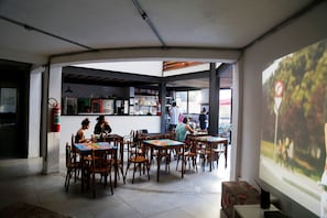 Un restaurante con mesas, sillas, una zona de cocina y una pantalla de proyección que muestra una imagen.