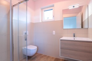 Features a glass shower enclosure, white toilet, and wooden vanity with a large mirror.