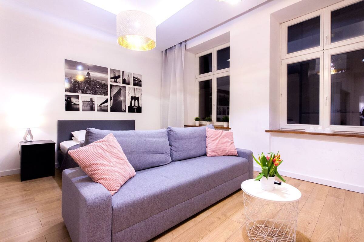 Una sala de estar moderna con un sofá gris, una mesita auxiliar y un ventanal con cortinas.