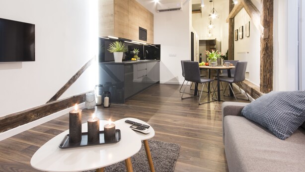 A modern living room with a sofa, a dining area with a table and chairs, a kitchen with a TV, and a staircase. - Aparthotel Floriańska 24 (Kraków)
