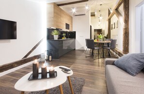 A modern living room with a sofa, a dining area with a table and chairs, a kitchen with a TV, and a staircase. - Aparthotel Floriańska 24 (Kraków)