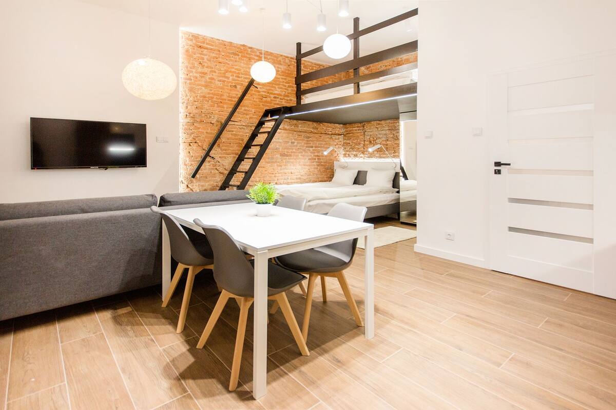 Un espacio habitable moderno con sofá, mesa de comedor, sillas, televisor, escalera y litera.