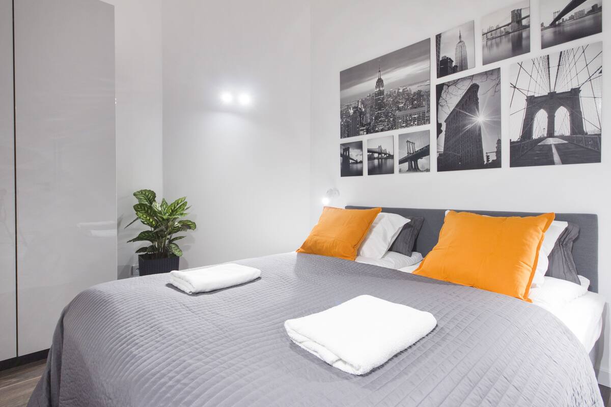 Una habitación de hotel moderna con una cama grande, ropa de cama gris y blanca, y un cuadro mural con vistas a la ciudad.