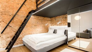 A modern bedroom with a brick wall, a bed, a mirror, and a staircase. - Aparthotel Floriańska 24 (Kraków)