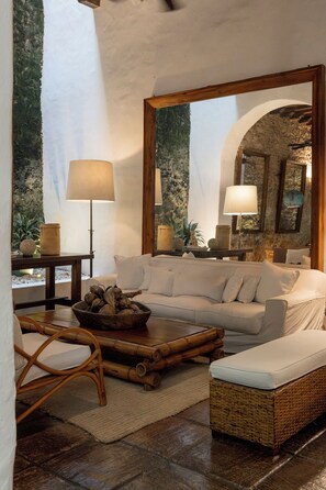 A cozy living room with a white sofa, a wicker bench, a coffee table with a bowl of nuts, and a large mirror reflecting the room. - Amarla Boutique Hotel Cartagena (Cartagena)