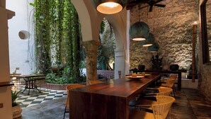 A restaurant with a long wooden table, wicker chairs, hanging lights, and a stone wall. - Amarla Boutique Hotel Cartagena (Cartagena)