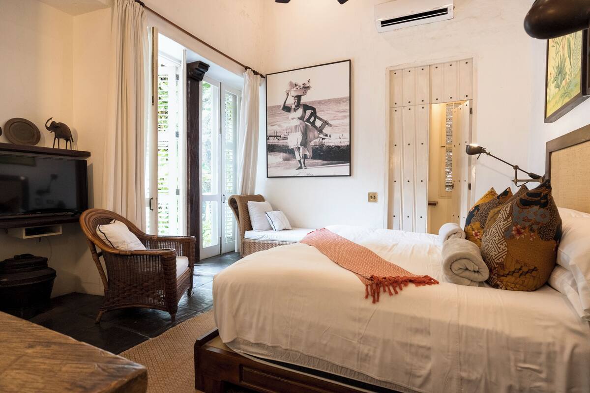 Un dormitorio con cama, una silla, un televisor y una puerta que da a un espacio exterior.