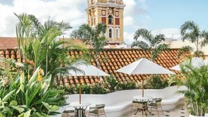 A pool area with a view of a church tower, surrounded by palm trees and outdoor seating. - Amarla Boutique Hotel Cartagena (Cartagena)