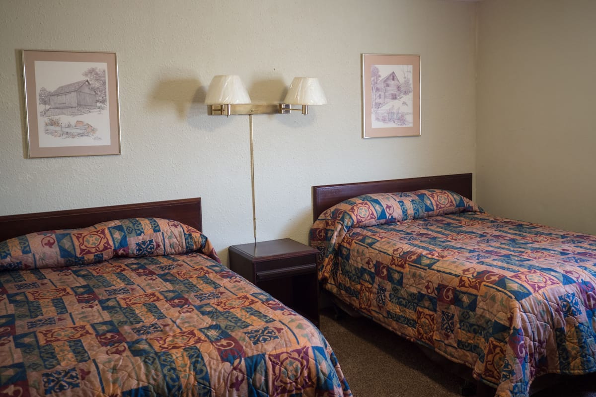 Una habitación de hotel con dos camas, una mesita de noche, una lámpara y dos cuadros en la pared.