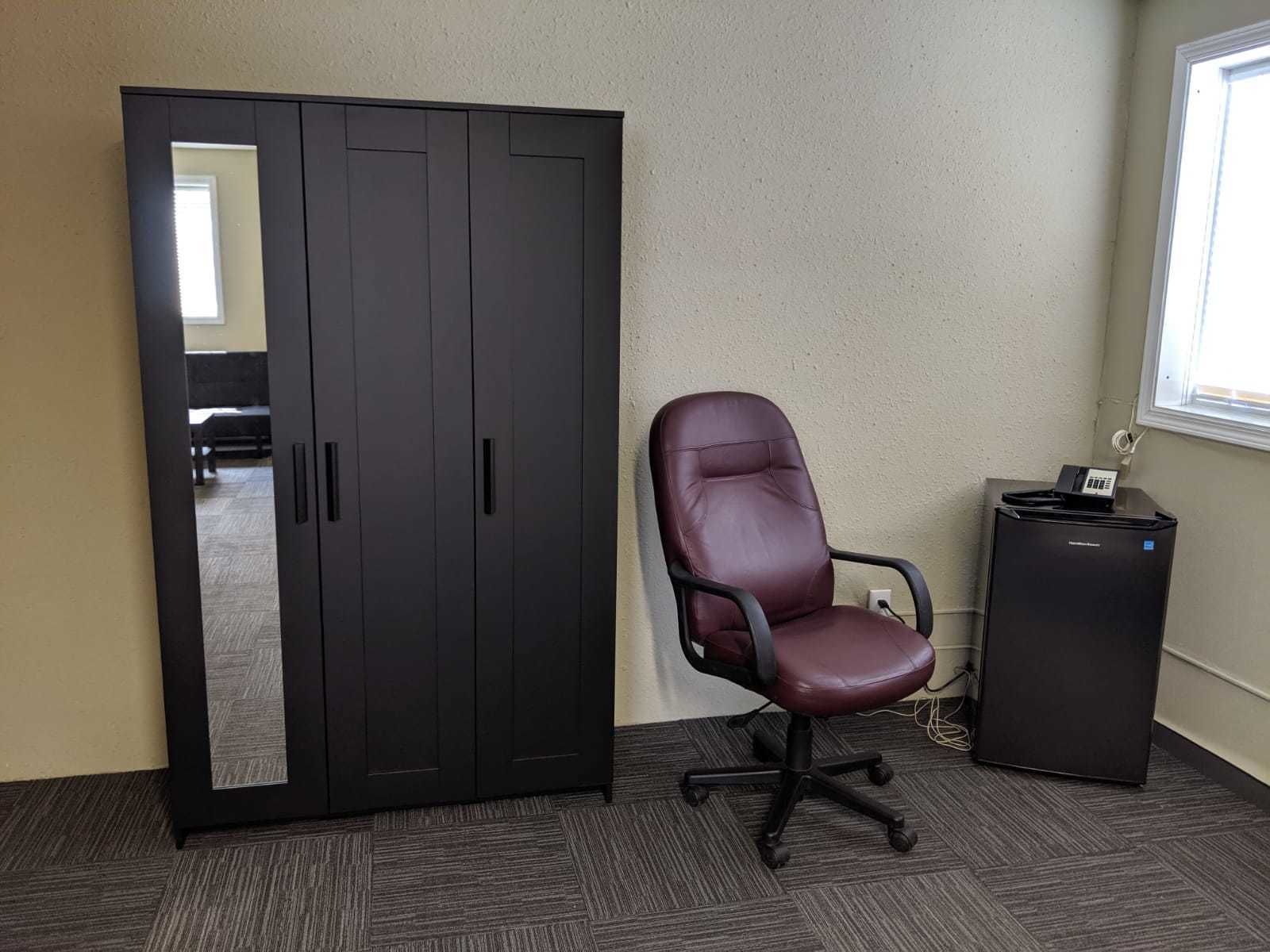 Una habitación con un armario grande, una silla de escritorio de cuero y un pequeño mueble negro.