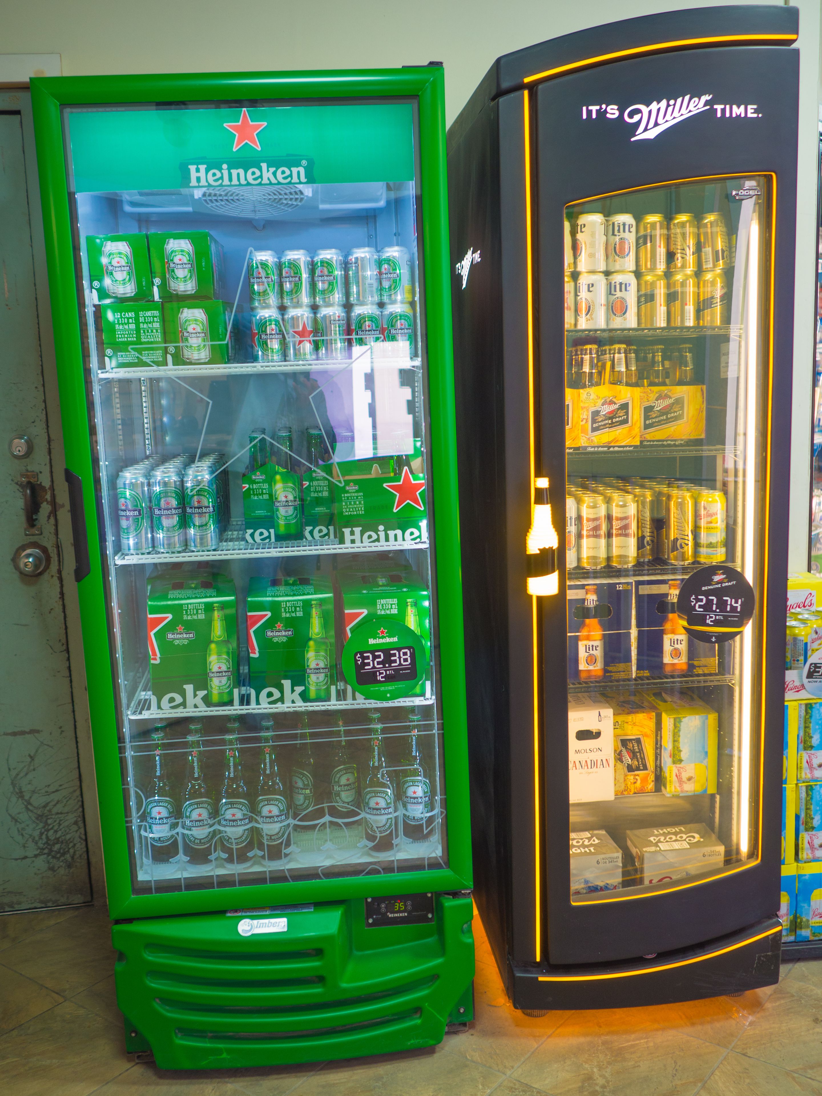 Two refrigerated beverage vending machines, one for Heineken and the other for Miller Lite, with various beer options and prices displayed.