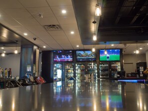 A bar area with multiple screens displaying sports events, a well-lit ceiling with hanging lights, and a polished floor. - The New Cavalier Inn (Winnipeg)