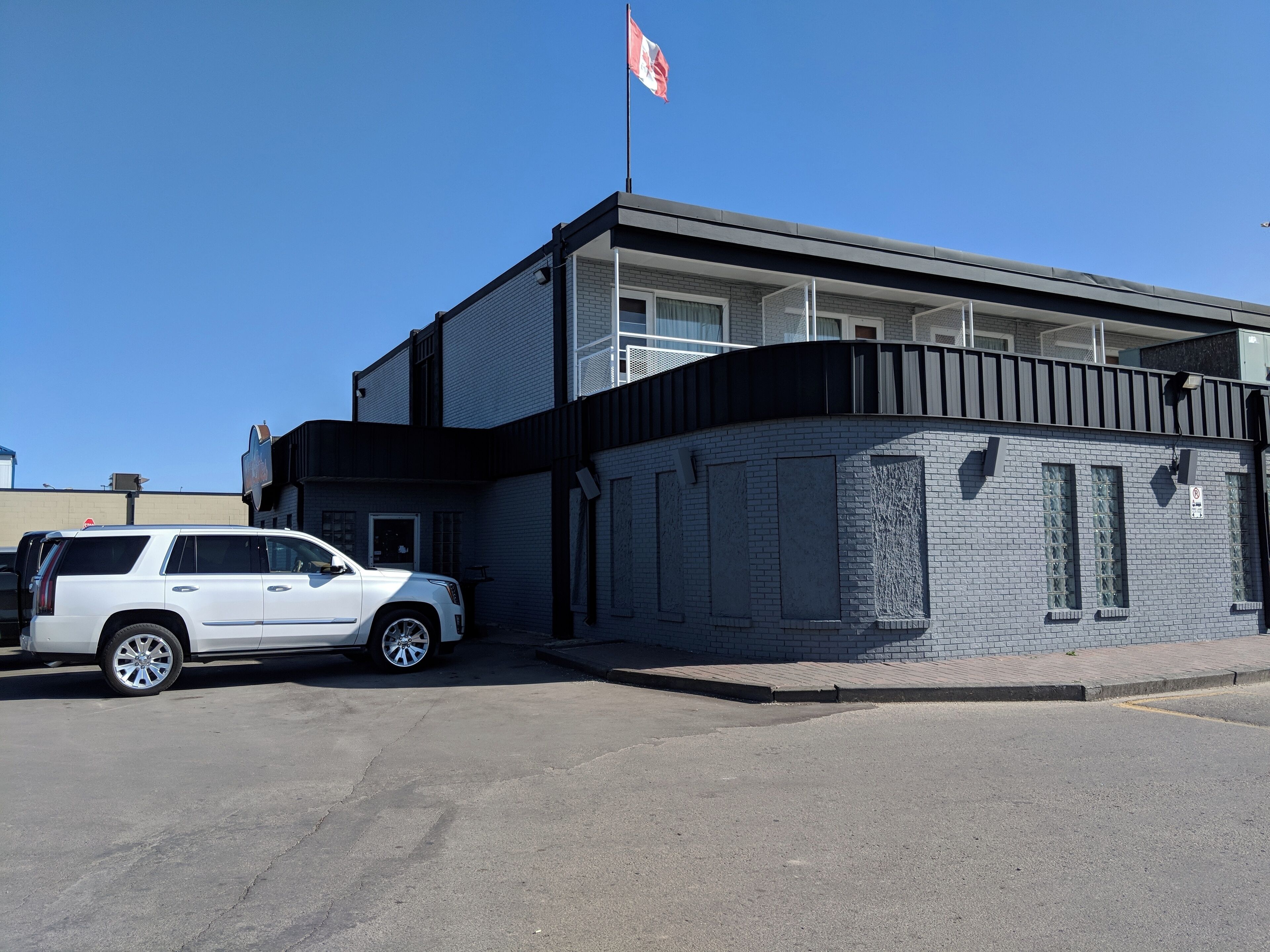 A building with a flag, a white SUV parked in front, and a clear blue sky.