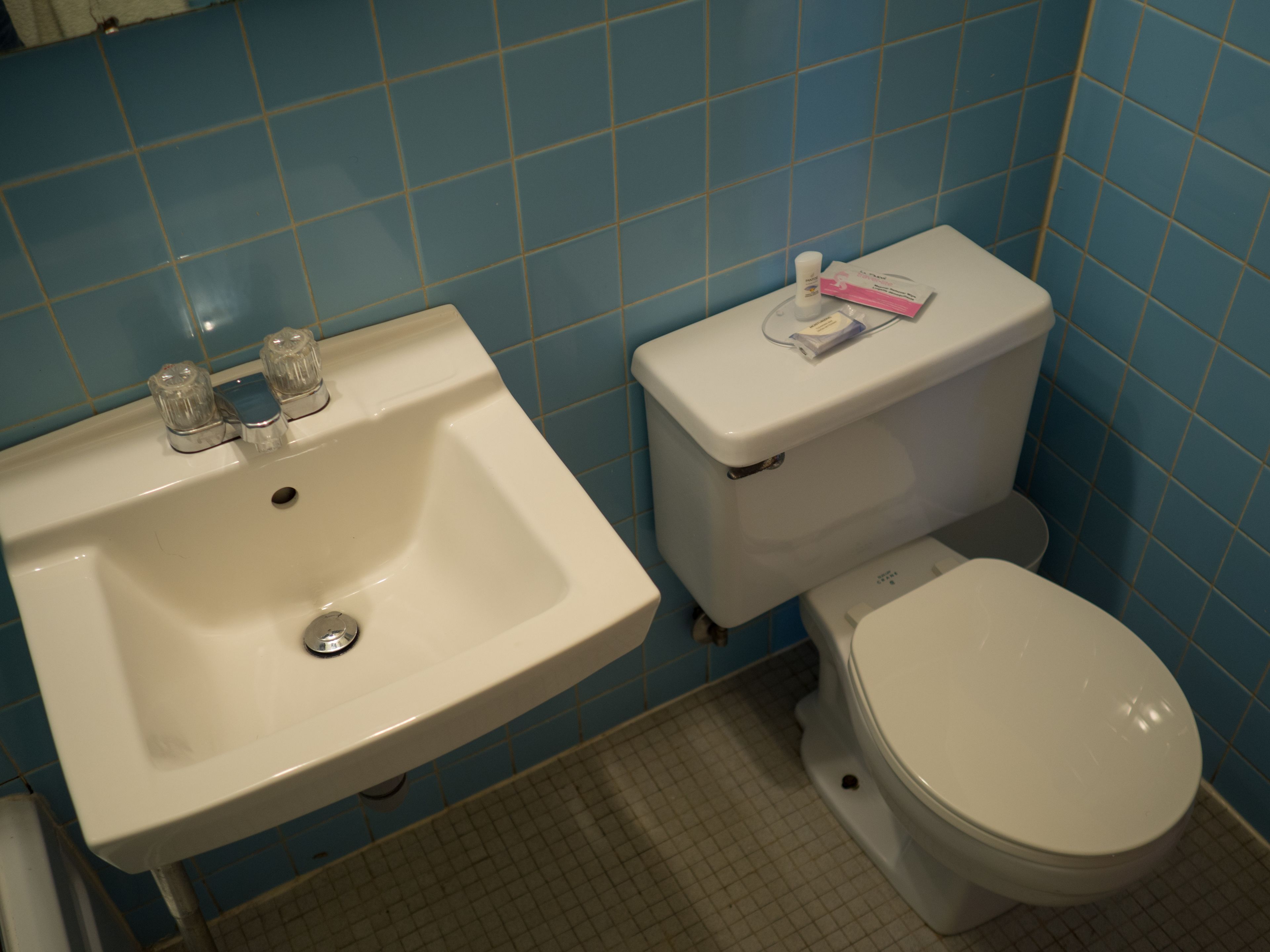 Et badeværelse med en hvid vask og toilet, blå flisevægge og et gulv med et gittermønster.