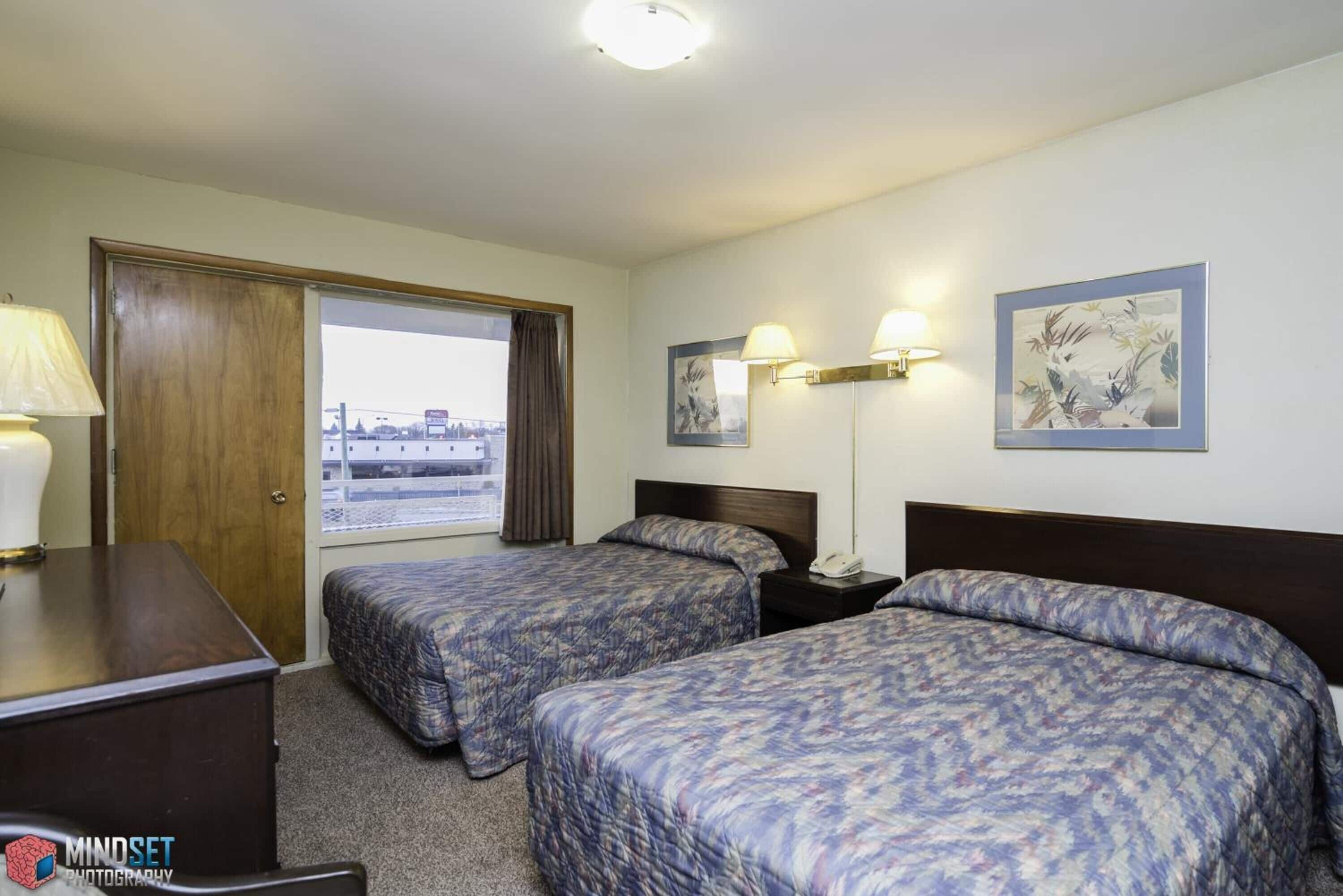 Habitación de hotel con dos camas, un escritorio, una lámpara y una ventana con vistas.