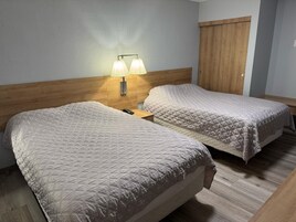 Habitación de hotel con dos camas, cabecero de madera, mesita de noche con lámpara y puerta de madera.