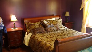 Un dormitorio con cama de madera, varios almohadones, una mesita de noche con lámpara y un aparador.