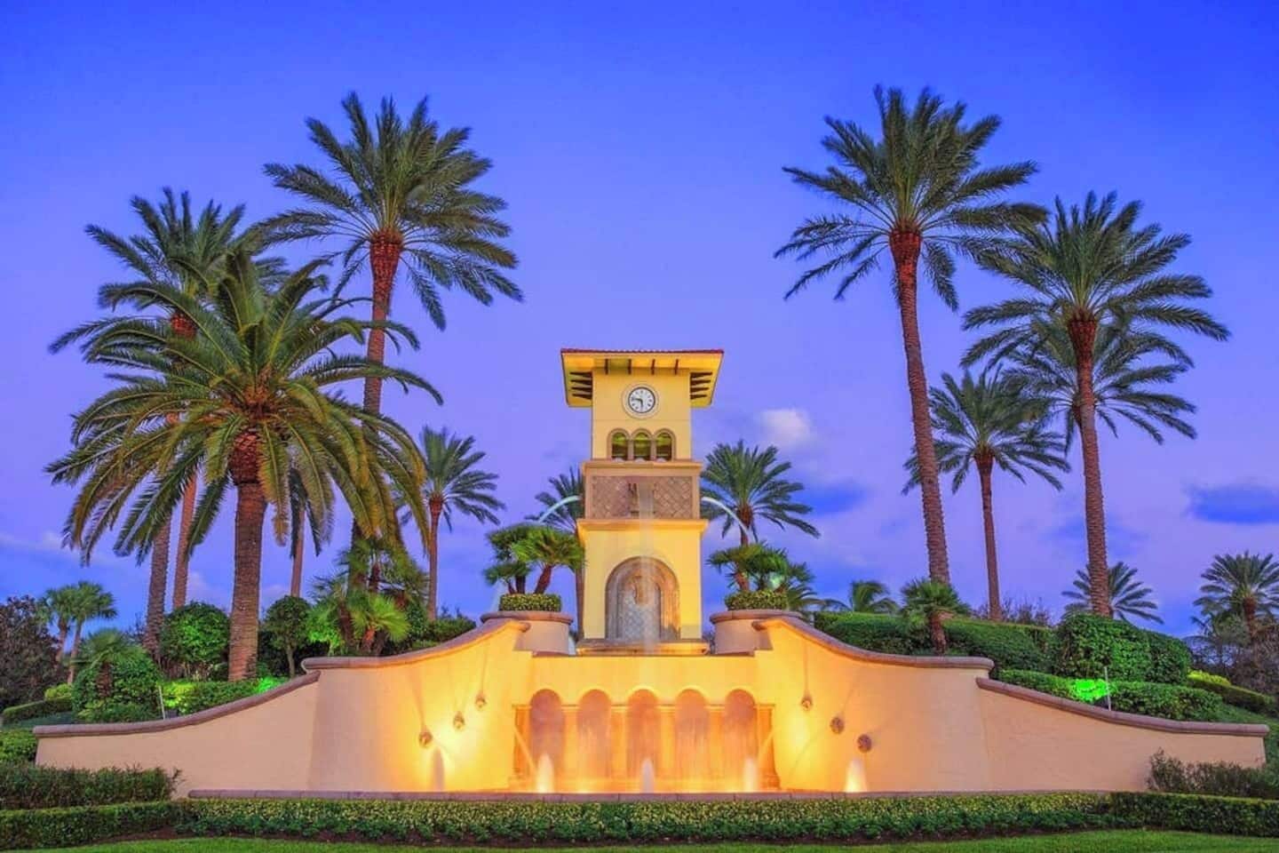 A clock tower with a clock face, surrounded by palm trees and a well-maintained garden.
