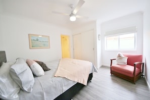 A bedroom with a bed, a chair, a ceiling fan, a window, and a door.