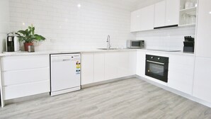 Uma cozinha moderna com armários brancos, lava-louças, micro-ondas e forno.
