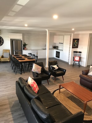 A modern living room with a black leather sofa, a wooden coffee table, and a dining area with a wooden table and chairs.