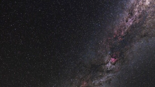 Una cabaña de madera con porche bajo un cielo estrellado, rodeada de follaje.
