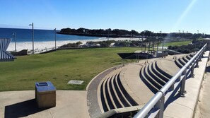 A stadium with tiered seating, a grassy field, and a beach in the background. - Oceanview 1 Bed Apartment @ Quality Resort Sorrento Beach (Sorrento)