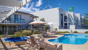 Un hotel moderno con piscina, zona de estar exterior y un letrero que indica Quality Resort.