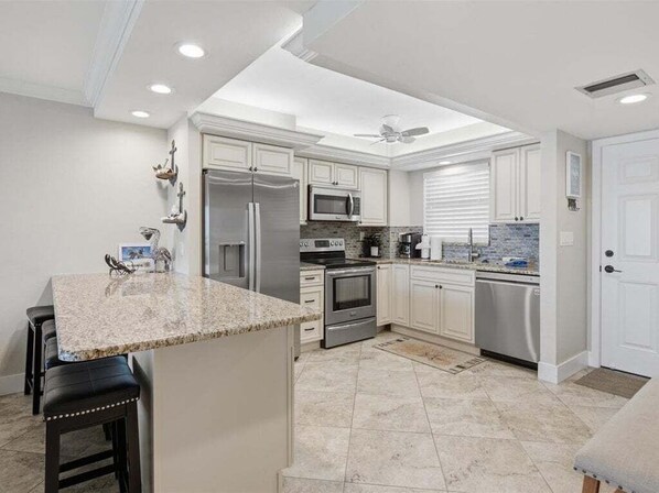 A modern kitchen with white cabinetry, stainless steel appliances, and a granite countertop. - Waterfront 2BR condo with pool, WiFi, and marina access in Marco Island. (Marco Island)