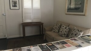 Una sala de estar con un sofá beige, una mesita de madera y una mesa de centro blanca con revistas.