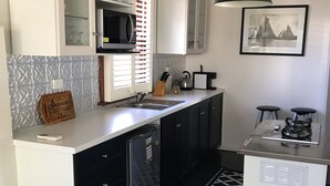 Una cocina moderna con armarios blancos, una encimera negra, un microondas, un hervidor y un refrigerador pequeño.