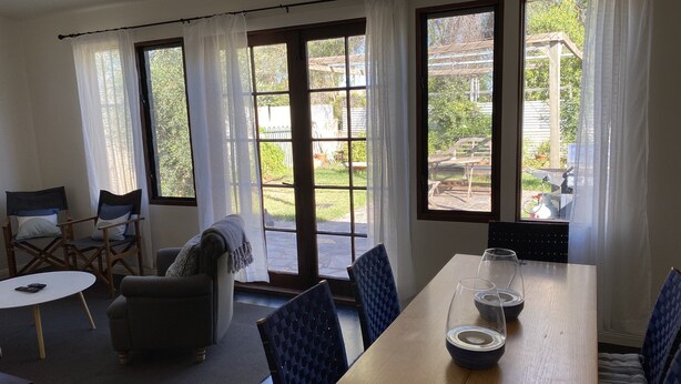 Un comedor con mesa de madera, sillas y vistas al jardín trasero a través de ventanas amplias.