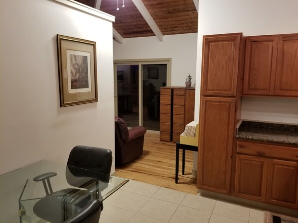 A dining area with a glass table, a black chair, wooden cabinets, and a framed picture on the wall.