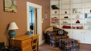 Ein gemütliches Zimmer mit einem karierten Sofa, einem kleinen Tisch mit Lampe und einem Bücherregal voller Bücher und Dekoration.
