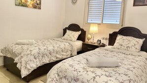 Ein Schlafzimmer mit zwei Betten, jeweils mit floralem Bettzeug und einem weißen Handtuch. Zwischen den Betten befindet sich ein Nachttisch mit einer Lampe und einer Uhr.