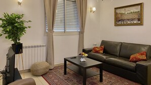 Ein Wohnzimmer mit Sofa, Couchtisch, Zimmerpflanze, Heizkörper und einem Bild an der Wand.