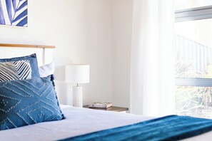 Ein ordentlich bezogenes Bett mit blauer Bettwäsche, eine Nachttischlampe und ein Buch auf dem Nachttisch.