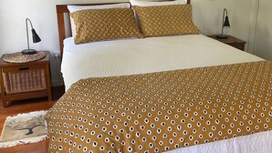 Un dormitorio con una cama grande, dos mesitas de noche, una lámpara de pared y una obra de arte enmarcada sobre la cama.