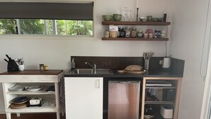 Cocina compacta con lavavajillas, pileta y microondas. Hay estantes sobre la mesada con distintos utensilios de cocina.