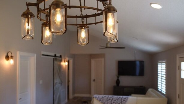 A modern living room with a white sofa, a TV mounted on the wall, and a chandelier with multiple light bulbs.