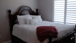 A bedroom with a wooden headboard, white bedding, and a red throw blanket.