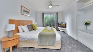 A hotel room with a bed, a bedside table with a lamp, a TV, a desk with a chair, and a view of the outdoors.