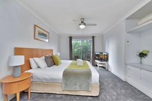 A hotel room with a bed, a bedside table with a lamp, a TV, a desk with a chair, and a view of the outdoors.