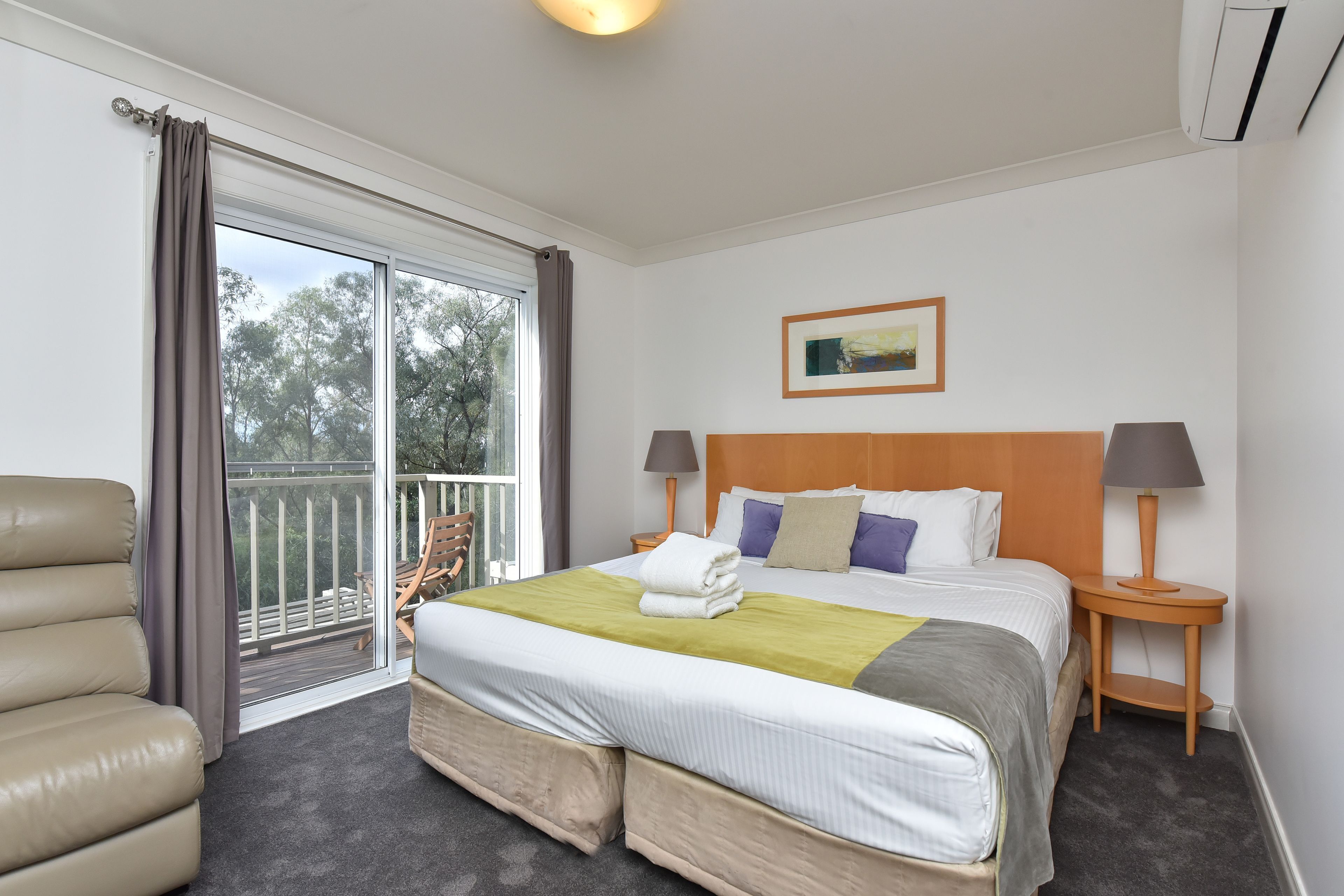 Une chambre d’hôtel avec un lit, deux tables de chevet, une chaise, une fenêtre avec des rideaux et un tableau au mur.