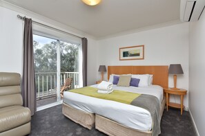 Une chambre d’hôtel avec un lit, deux tables de chevet, une chaise, une fenêtre avec des rideaux et un tableau au mur.