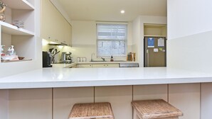 Une cuisine moderne avec un plan de travail blanc, des appareils en acier inoxydable et une fenêtre équipée de stores.