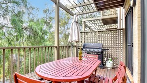 A covered outdoor patio with a red table and benches, a grill, and a bottle of wine.